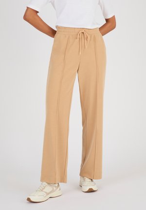 Beige weite Hosen mit elastischem Bund und Kordelzug, kombiniert mit weißen Sneakers und einem weißen kurzärmligen Oberteil.