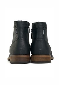 Black vegan leather ankle boots with a textured surface, a rear zipper, and a brown wooden heel. Features decorative stitching and branding.