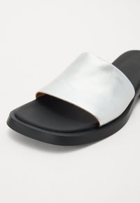 Srebrni metalik klizni sandal s širokom trakom, crnom teksturiranom potplatom i zaobljenim rubovima za elegantan izgled.