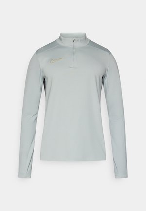 Gaiši pelēks garām piedurknēm tops ar stāvošu apkakli, rāvējslēdža plākstera un zelta Nike logotipu krūšu rajonā, izgatavots no gludas, elastīgas auduma.