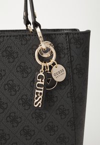 Sac à main noir texturé avec des accessoires en métal doré, présentant des charmes de logo et un design structuré. Comprend des poignées doubles et des motifs subtils.