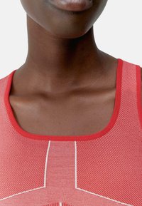 Rotes sportliches Tanktop mit einem strukturierten Muster, das weiße Nähte und einen runden Ausschnitt aufweist, vor einem neutralen Hintergrund präsentiert.