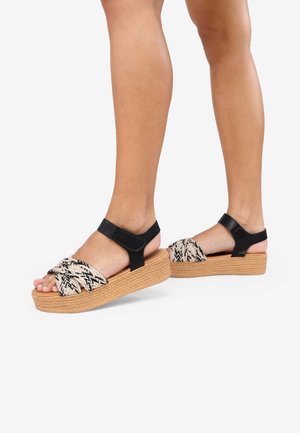 Sandalias de plataforma con una cinta sintética negra, parte superior tejida en beige y negro, y una suela texturizada estilo yute.