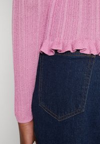 Roze geribbelde gebreide trui met een gerimpelde zoom, gecombineerd met donkerblauwe denim jeans met een achterzak en zichtbare stiksels.