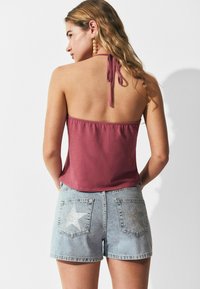 Top halter burdeos con un diseño de cuello atado, combinado con shorts de mezclilla claros que presentan adornos de estrellas plateadas en los bolsillos traseros.