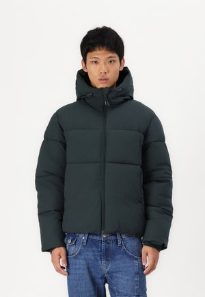 Donkergroene pufferjack met een capuchon, ritssluiting en een doorgestikt ontwerp. Heeft elastische boorden en een verkorte snit. Casual denim jeans.