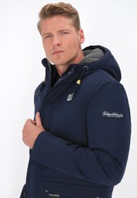 Námornícky modrá mikina s kapucňou, so šedým fleece podšívkou, so zapínaním na zips a vyšitým logom na rukáve; obsahuje sťahovacie šnúrky a praktické vrecká.