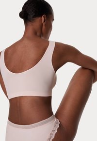 Bralette sin costuras de color rosa claro con tirantes anchos y textura suave, combinado con braguitas a juego con encaje en los bordes, mostrando una vista de perfil.