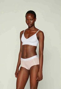 Bela braleta z tankimi naramnicami in gladko teksturo, v kombinaciji z svetlo rožnatimi hlačkami hipster, ki imajo pas s napisom.