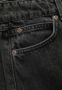 Sorte denim jeans med en struktureret overflade, kobbernitter og en lille forlommem tilføjer et fokus på holdbarhed og stil i designet.