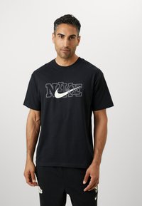 Černé bavlněné tričko s velkým bílým logem Nike a vrstveným designem textu "NIKE". Klasický kulatý výstřih a krátké rukávy.