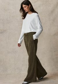 Witte gebreide trui met lange mouwen, gecombineerd met olijfgroene wijde corduroybroek. Casual pasvorm met een elastische trekkoord in de taille.