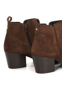Brown suede ankle boots with a block heel, featuring a side zipper and pull tabs. The upper has a smooth texture and minimal stitching detail.