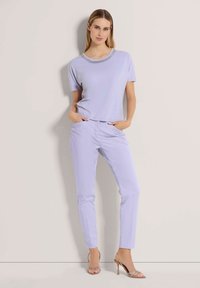 Lichtpaarse top met korte mouwen en een bewerkte halslijn, gecombineerd met bijpassende lichtpaarse slim-fit broek en sandalen met hoge hakken en bandjes.