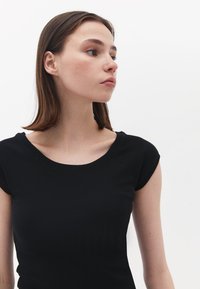 T-shirt nero a costine con scollo a barca e maniche a cappuccio corte, caratterizzato da un design aderente e una texture liscia.
