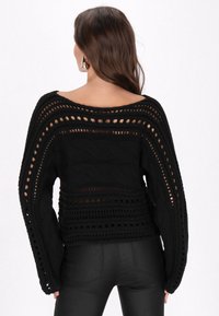 Maglione nero lavorato a maglia con un design a punto aperto, ampia scollatura a barca e maniche lunghe ampie e morbide. Motivi a treccia testurizzati su tutta la superficie.