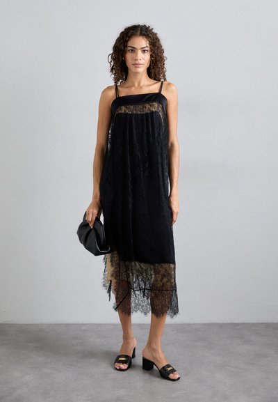 Μαύρο φόρεμα δαντέλας με διάφανη επικάλυψη και κροκοδειλέ hem, λεπτές τιράντες και επιμερισμένο σχέδιο. Συνδυάζεται με μαύρες σανδάλες με τετράγωνο τακούνι και μια τσάντα-χυμού.