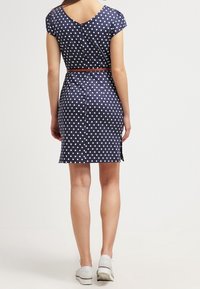 Mörkblå prickig klänning med åtsittande midja, korta ärmar och V-ryg, avslutad med ett smalt bälte och bärs med vita sneakers.