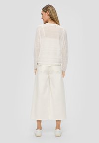 Top bianco leggero a maniche lunghe con un design a righe texturizzato abbinato a pantaloni bianchi a gamba larga e sneakers bianche casual.