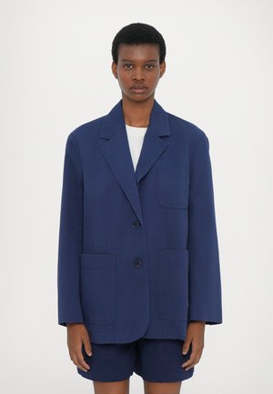 Blazer azul-marinho feito de algodão, com lapela picada, dois bolsos frontais e fecho de botão único. Combinado com calções a condizer.
