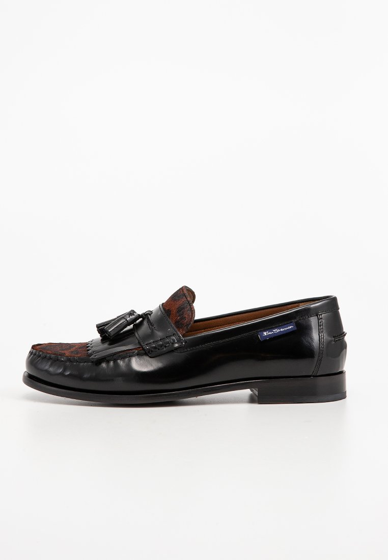 Mocassino in pelle nera con un motivo marrone testurizzato nella parte anteriore, caratterizzato da un accento con nappina e un tacco basso e slanciato.