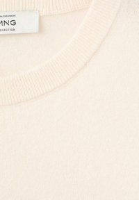 Maglione in cashmere di colore beige chiaro, caratterizzato da un colletto a girocollo a coste e una texture morbida. Etichetta di cura parzialmente visibile sul colletto.