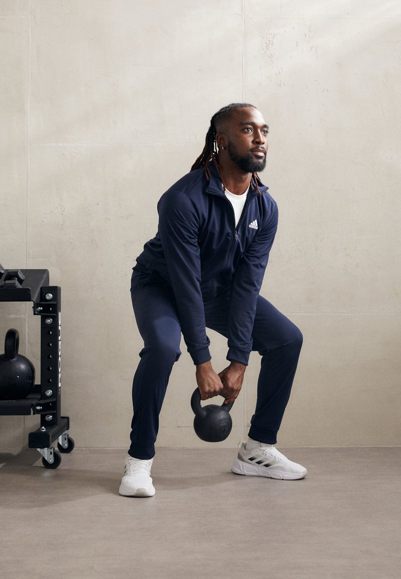 Chandales deportivos en color navy con acentos blancos, pesa rusa negra y zapatillas blancas. Textura suave, diseño ajustado y funcional para entrenamientos.