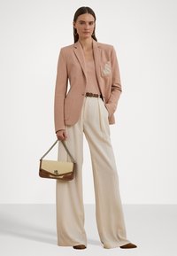 Blazer rose clair avec une patch, débardeur beige et pantalon large crème. Les accessoires incluent un petit sac à main marron et beige avec une bandoulière en chaîne.