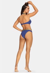 Niebieski komplecik bikini z halterem i niskim stanem, ozdobiony plecionym, wielobarwnym paskiem wokół talii. Gładka faktura materiału.