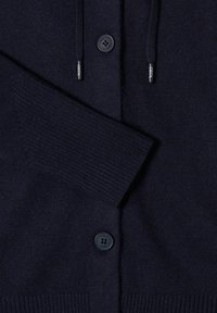 Cardigan blu navy con una texture a maglia, dotato di due bottoni e lacci. Le maniche e l'orlo a coste offrono un ulteriore dettaglio.