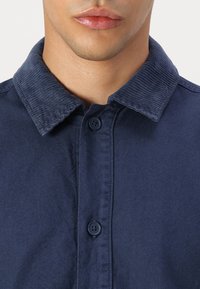 Navy blue shirt featuring a corduroy collar, button-down closure, and a smooth texture. Crisp fabric with a structured design.