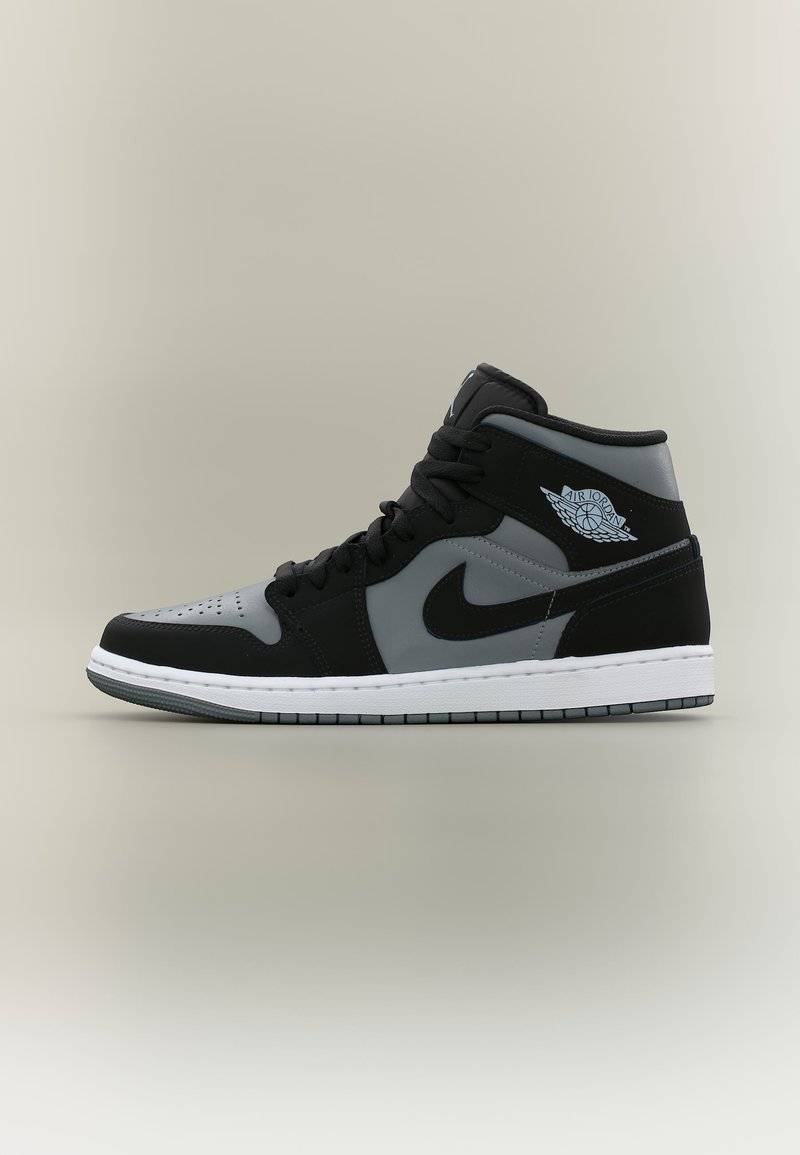 Μαύρο-γκρι αθλητικό παπούτσι Air Jordan μέτριου ύψους με μαύρα κορδόνια, λογότυπο Nike και λευκή σόλα, εμφανίζεται πλευρικά σε ουδέτερο φόντο.