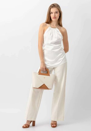 Haut en satin blanc à encolure halter, pantalon beige ajusté, sandales à talons marron et sac à main géométrique en crème et tan avec une anse.