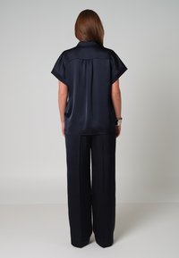 Navy zijden blouse met korte mouwen, losse pasvorm en een plooitje aan de achterkant. Gecombineerd met bijpassende wijde broek, wat een strakke, minimalistische uitstraling geeft.