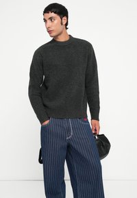 Dark gray knitted sweater with a ribbed texture, round neck, and long sleeves, paired with blue pinstriped wide-leg trousers.
