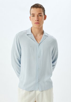 Lysblå kortærmet button-up skjorte med blød tekstur, kravesdesign og lige kant. Modellen har cremefarvede bukser på.