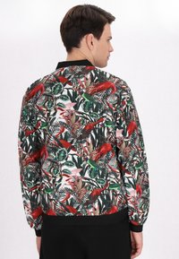 Giacca bomber floreale in tessuto leggero con un vivace motivo tropicale rosso e verde. Collo e polsini a costine neri.