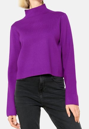Jersey de cuello alto morado, diseño corto, mangas largas, textura suave, llevado con pantalones vaqueros negros.