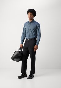 Sinine triibuline särk, mustad püksid ja läikivad mustad kingad. Modell kannab musta nahast duffel-kotti. Siledad tekstuurid ja kaasaegne disain.