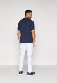 Ναυτικό πόλο μπλουζάκι, κοντά μανίκια, με στρογγυλή κολάρα, σε συνδυασμό με λευκά παντελόνια και μπλε αθλητικά παπούτσια. Απλός σχεδιασμός, casual εφαρμογή.