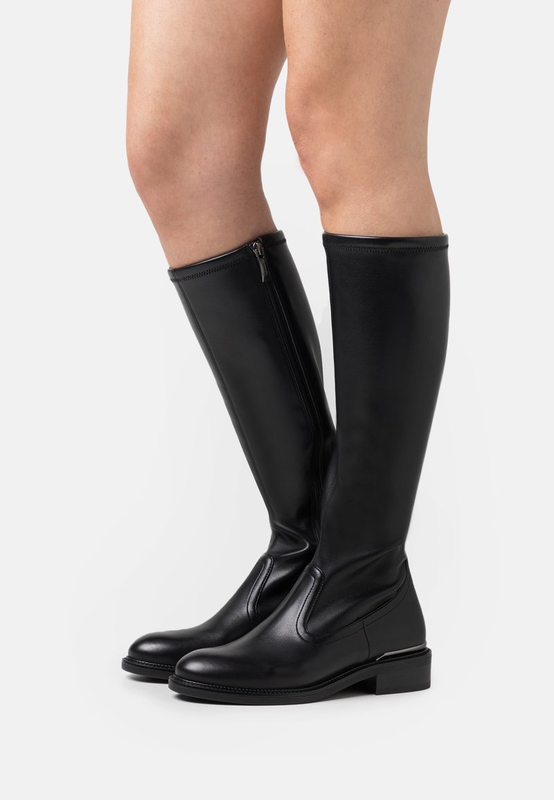 Bottes hautes en cuir noir jusqu'aux genoux avec fermeture éclair latérale, portées sur des jambes nues, dotées de talons blocs bas et d'orteils arrondis.