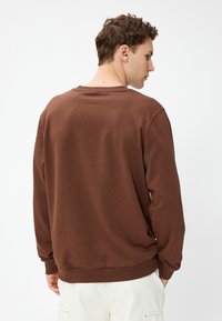 Brązowa bluza z okrągłym dekoltem, długimi rękawami i lekko teksturowanym materiałem. Posiada ściągacze na mankietach i dole. Prosty design.