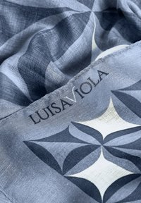 Bufanda azul y gris con patrón geométrico, textura suave y etiqueta que dice "LUISA VIOLA".