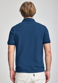 Marineblaues Poloshirt mit kurzen Ärmeln, flachem Kragen und feiner Textur. Es zeichnet sich durch ein sauberes Design mit geradem Saum und minimaler Details aus.
