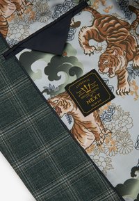 Giacca slim-fit con materiale esterno a quadri verdi, foderata con un motivo che mostra tigri e design floreali, etichetta dettagliata visibile.
