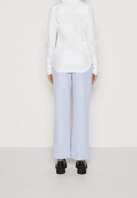 Camicia bianca a maniche lunghe con orlo curvo, abbinata a pantaloni larghi blu chiaro e scarpe platform nere spesse.