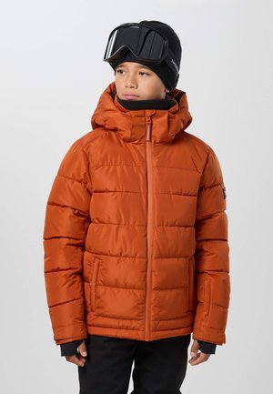 Enfant portant une doudoune orange, un pantalon de ski noir, un bonnet noir et des lunettes de ski, regardant légèrement sur le côté.