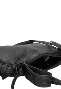 Sac en cuir noir avec une surface texturée, doté d'une fermeture zippée et d'une sangle ajustable. Intérieur visible avec un revêtement sombre.