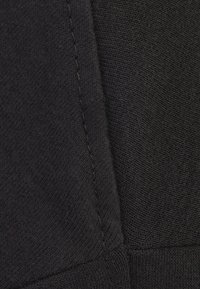 Svart tyg har en slät yta med synliga sömmar. Designen inkluderar en paneluppbyggnad som visar på olika nyanser av svart.