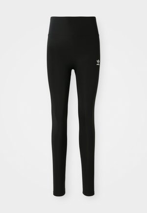 Black leggings made of stretchy material with a high waist, featuring a small white Adidas logo on the left leg. Smooth texture.